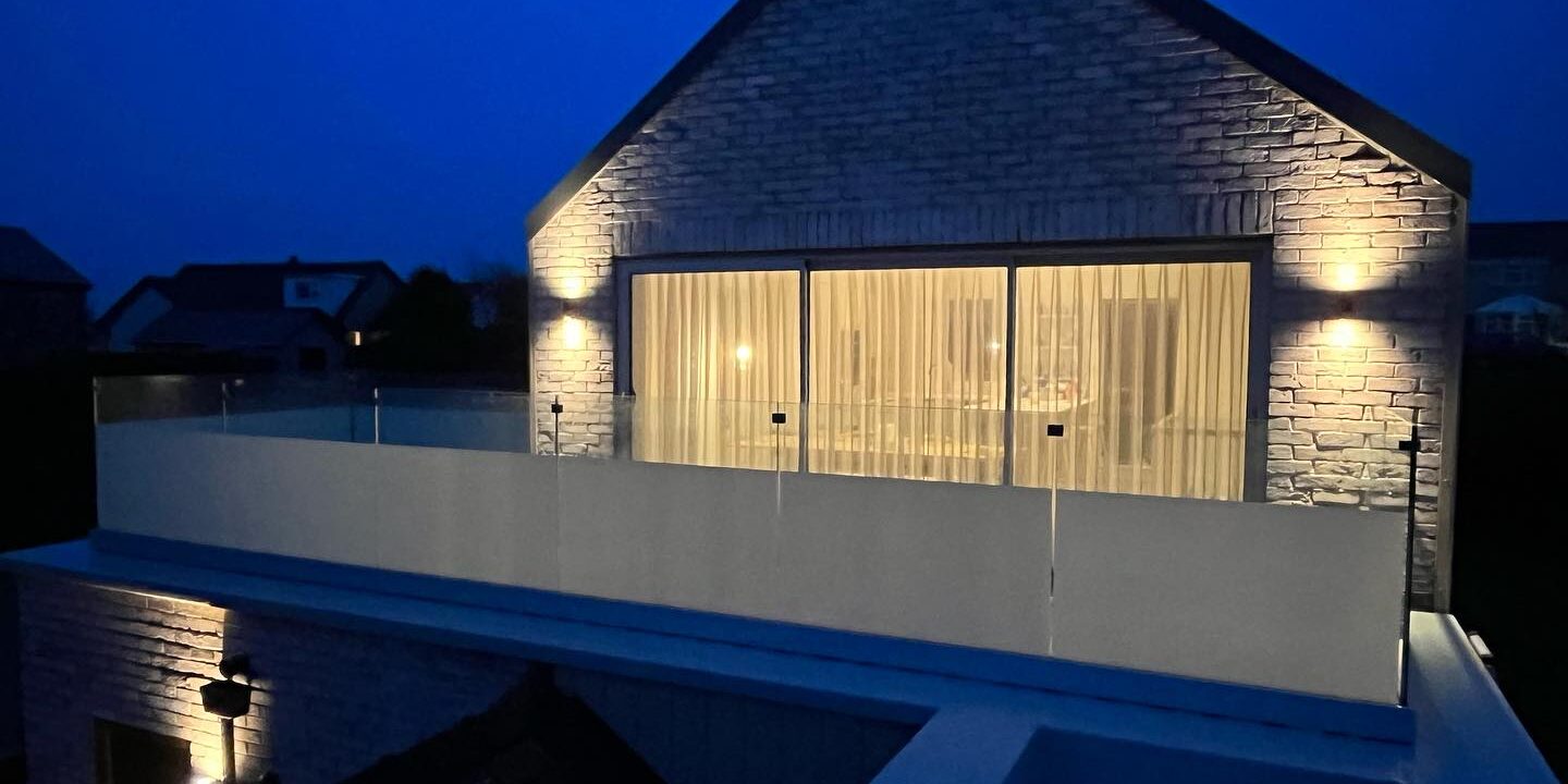 frame-one Image of a newly installed frameless glass balcony in Rhosneigr, Anglesey, featuring 21.5mm toughened laminated glass with partial frosting, overlooking a scenic coastal view
