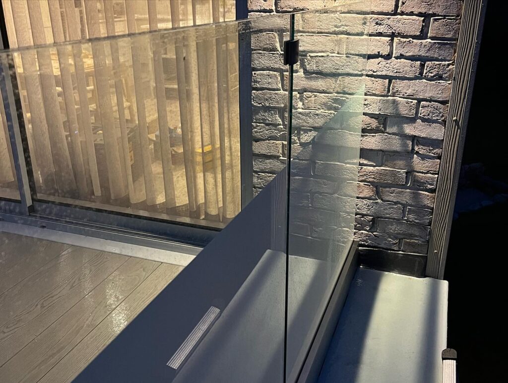 Close-up view highlighting the intricate details of the 21.5mm toughened laminated glass and the watertight fixing positions on the frameless balcony in Rhosneigr, Anglesey