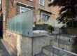 Glass balustrade installation in Salford featuring 17.5mm toughened laminated glass panels with structural spigots and aluminium capping rail by NW Fabrications